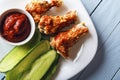 Baked chicken wings, tomato paste and sliced cucumbers on a white plate on a wooden table. Top view from above. Copy space for tex Royalty Free Stock Photo