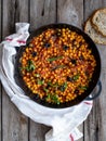 Baked chickpea with vegetables, olives and sun-dried tomatoes in iron pan, frying pan on wooden table. Vegan vegetarian