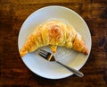 Baked croissant in white plate with fork on wood table restaurant background Royalty Free Stock Photo