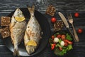 Baked Dorado fish on a black plate, salad with tomato mozzarella and lettuce leaves. Royalty Free Stock Photo