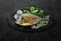 Baked Dorado fish with vegetables on a black stone plate. Top view.