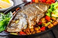 Baked dorado fish with vegetables and lemon on pan on wooden background close up. Royalty Free Stock Photo