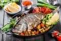 Baked dorado fish with vegetables and lemon on pan on wooden background close up. Royalty Free Stock Photo