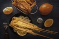 Baked fish on skewers in a black plate, french fries and lemon on a wooden table. Royalty Free Stock Photo