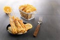 Baked fish on skewers in a black plate, french fries and lemon on a wooden table. Royalty Free Stock Photo