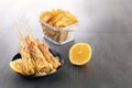 Baked fish on skewers in a black plate, french fries and lemon on a wooden table. Royalty Free Stock Photo