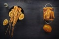 Baked fish on skewers in a black plate, french fries and lemon on a wooden table. Royalty Free Stock Photo