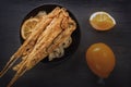 Baked fish on skewers in a black plate and french fries on a wooden table. Royalty Free Stock Photo