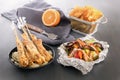 Baked fish on skewers in a black plate, vegetables in foil, french fries and lemon on a wooden table. Royalty Free Stock Photo
