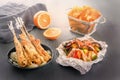 Baked fish on skewers in a black plate, vegetables in foil, french fries and lemon on a wooden table Royalty Free Stock Photo