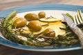 Baked green asparagus, sliced lemon, olives, and seasoning close up on a plate
