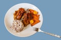 Baked hen with carot and kumquat, rice with quinoa on white plate on blue