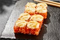 Baked Maki sushi on dark slate. Hot california maki with cheese. Sushi roll with tobiko outside, baked cheese topped. Style