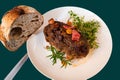 Baked meatloaf and herb twig on white plate, bread and knife on green background