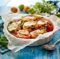 Baked multi-colored bell peppers stuffed with bulgur with dried tomatoes, herbs and cheese in a baking dish on a blue table. Royalty Free Stock Photo