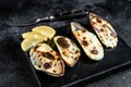 Baked mussels with cheese and lemon in shells. Black background. Top view