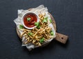 Baked parsnips french fries and homemade ketchup on cutting board - healthy vegetarian snacks on dark background