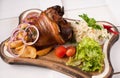 Baked pork knuckle with sauerkraut, potatoes, onions and greens on a wooden cutting board