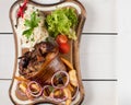 Baked pork knuckle with sauerkraut, potatoes, onions and greens on a wooden cutting board. View from above