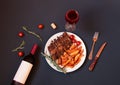 Baked pork ribs on plate with roasted potatoes, glass of red wine, bottle of red wine, rosemary and cherry tomatoes near