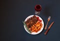 Baked pork ribs on plate with roasted potatoes, rosemary and cherry tomatoes and glass of red wine near on dark background. Royalty Free Stock Photo