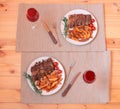 Baked pork ribs on plates with roasted potatoes, rosemary and cherry tomatoes and glasses of red wine near on wooden table. Royalty Free Stock Photo