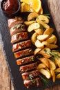 Baked pork tenderloin with rosemary in honey-orange sauce served with potato wedges closeup on a plate. Vertical top view Royalty Free Stock Photo