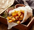 Baked potato fries, wedges with addition sea salt and rosemary on a wooden background.