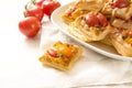 Baked puff pastry snacks with cream cheese, tomatoes and herb pesto, party finger food served on a white napkin and a plate at a Royalty Free Stock Photo