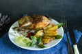 baked quail with potatoes and vegetables on plate on dark background