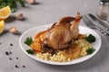 Baked quails with lemon and orange served with bulgur on a white plate on a gray background, Closeup. Royalty Free Stock Photo