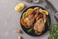 Baked quails with lemon and orange served on a dark plate on a gray background, Copy space