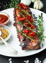 Baked ribs on a plate. Roasted ribs with spices and herbs on a dark background. Food background. Side view. Close-up