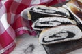 Baked roll with poppy seeds, three chopped pieces close-up on a wooden background with a red and white cloth.