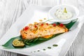 Baked salmon with cheese sauce, rosemary and lemon on wooden background. Hot fish dish.