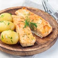 Baked salmon in creamy sauce with young boiled potato topped with melted butter and chopped dill on wooden plate, square format