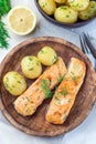 Baked salmon in creamy sauce with young boiled potato topped with melted butter and chopped dill on wooden plate, vertical, top