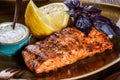 Baked salmon fillet with cheese sauce, basil and lemon on plate on wooden background. Royalty Free Stock Photo