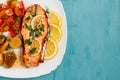 Baked salmon fillet medallion with salad of pickled vegetables and mushrooms on a white plate on a blue background, top view,