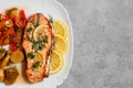 Baked salmon fillet medallion with salad of pickled vegetables and mushrooms on a white plate on a gray background, top view,