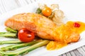 Baked salmon garnished with physalis, asparagus, tomatoes with herbs on wooden background. Royalty Free Stock Photo