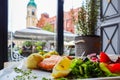 Baked salmon with mashed potatoes, lemon, tomatoes, red onions, olives and salad leaves on a background of historical buildings of Royalty Free Stock Photo
