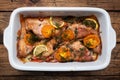 Baked sea bass with tomato pepper lemon and herbs in a ceramic baking sheet on a wooden background. Fish cooked in a home oven on Royalty Free Stock Photo