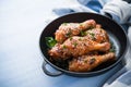 Baked spicy chicken legs with sesame and parsley in cast iron frying pan on blue wooden background