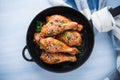Baked spicy chicken legs with sesame and parsley in cast iron frying pan on blue wooden background top view