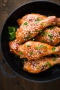 Baked spicy chicken legs with sesame and parsley in cast iron frying pan on dark wooden background