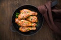 Baked spicy chicken legs with sesame and parsley in cast iron frying pan on dark wooden background