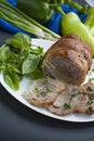 Baked stuffed roll with greens served on a white plate. Dark background