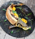 Baked sturgeon fish with rosemary, lemon and passion fruit on plate on wooden background close up.