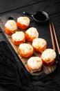 Baked sushi maki rolls with salmon, crab, cucumber, avocado, flying fish roe and spicy sauce, on black wooden table background Royalty Free Stock Photo